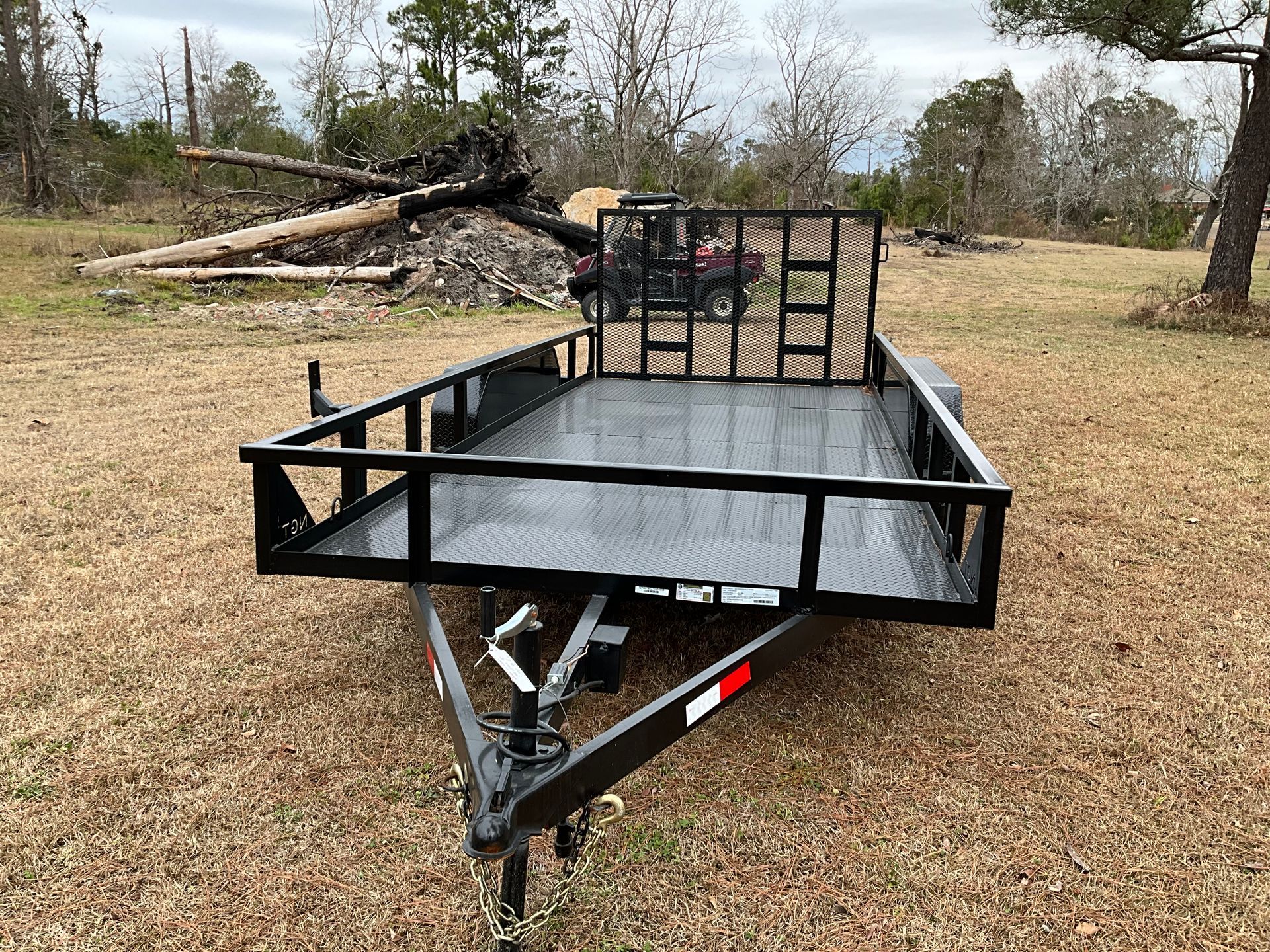 A black utility trailer with a mesh ramp sits in a grassy field.