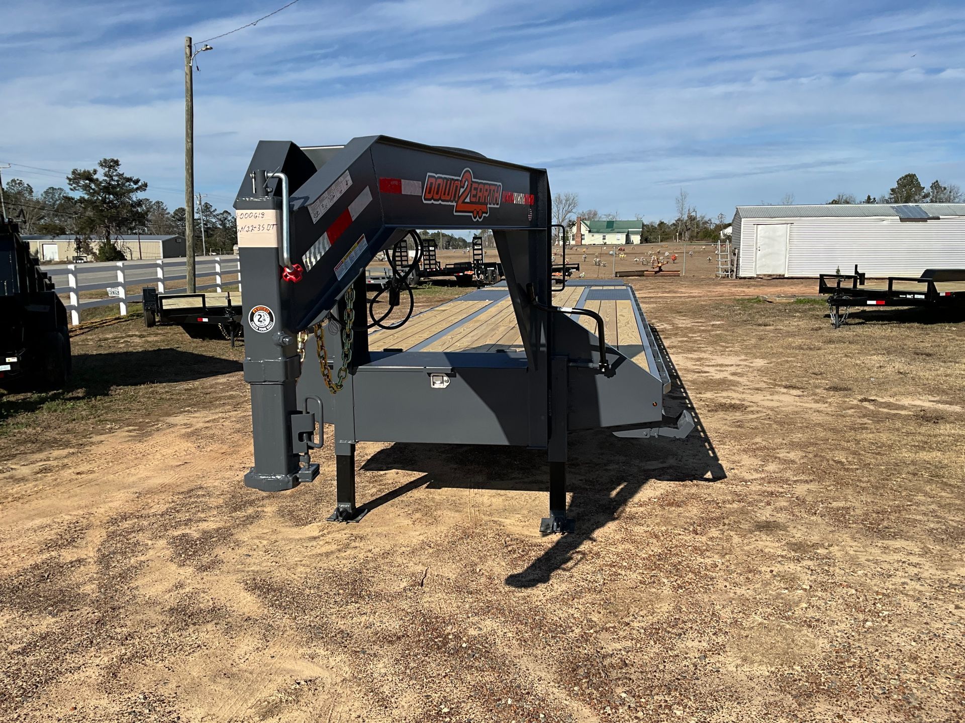 A dark gray gooseneck trailer neck parked on a dirt lot on a sunny day.