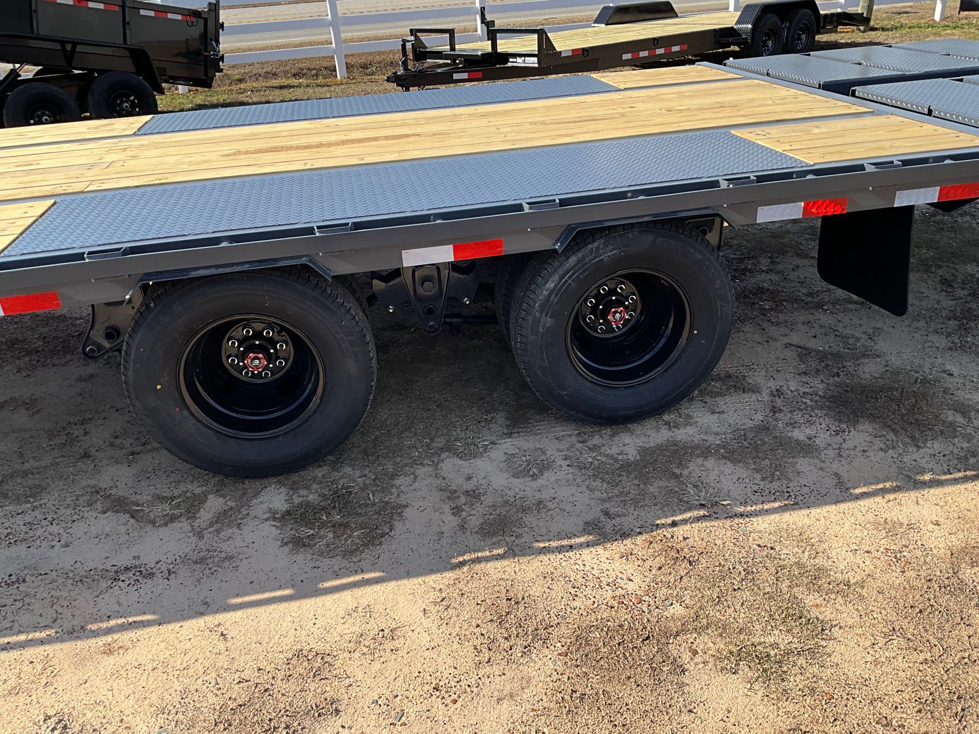 A side view of a flatbed trailer with two black tires, a wood and metal deck, and red safety reflectors.