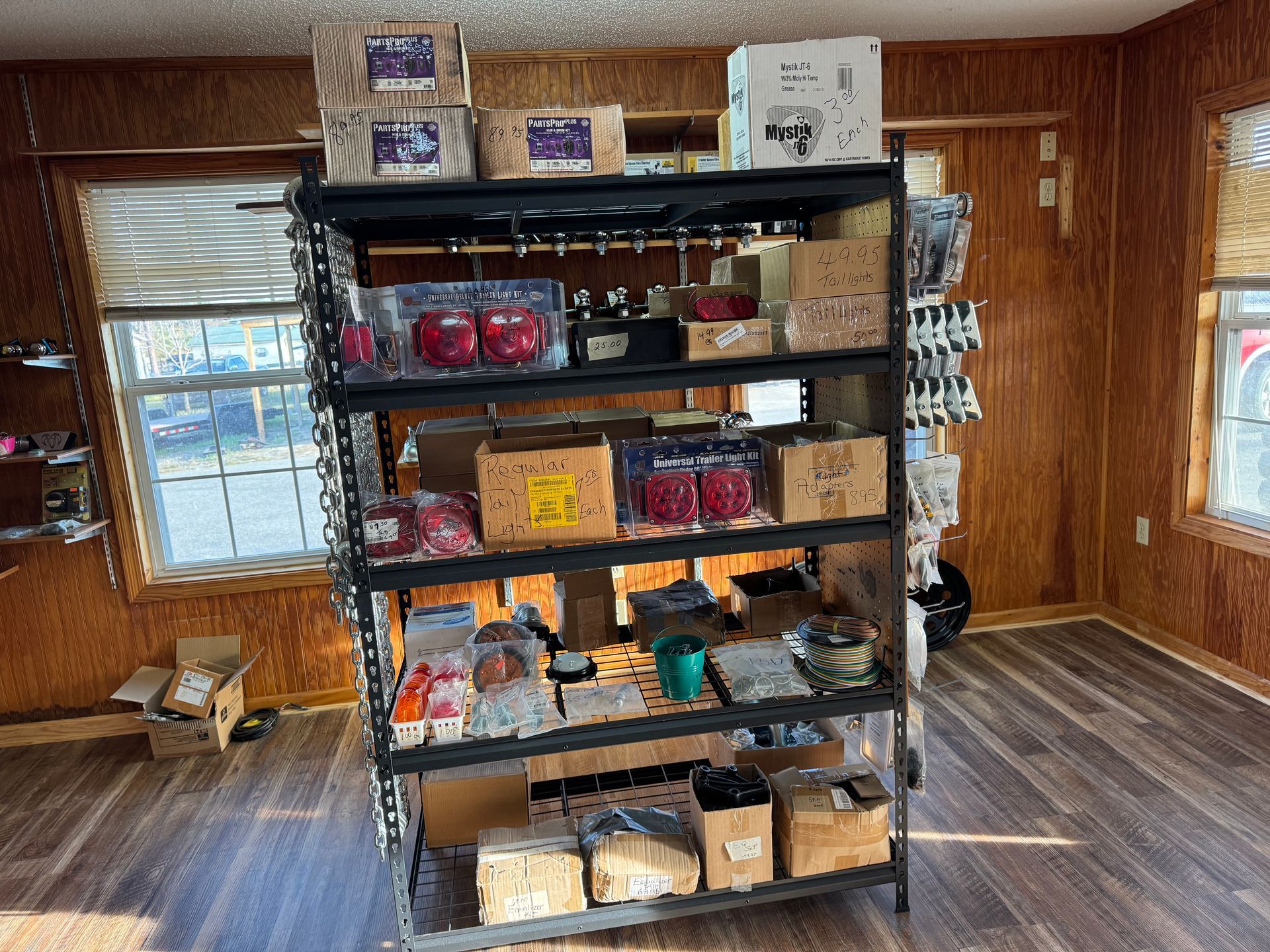 A black metal shelving unit filled with various cardboard boxes and retail items sits on a wood-look floor in a room.