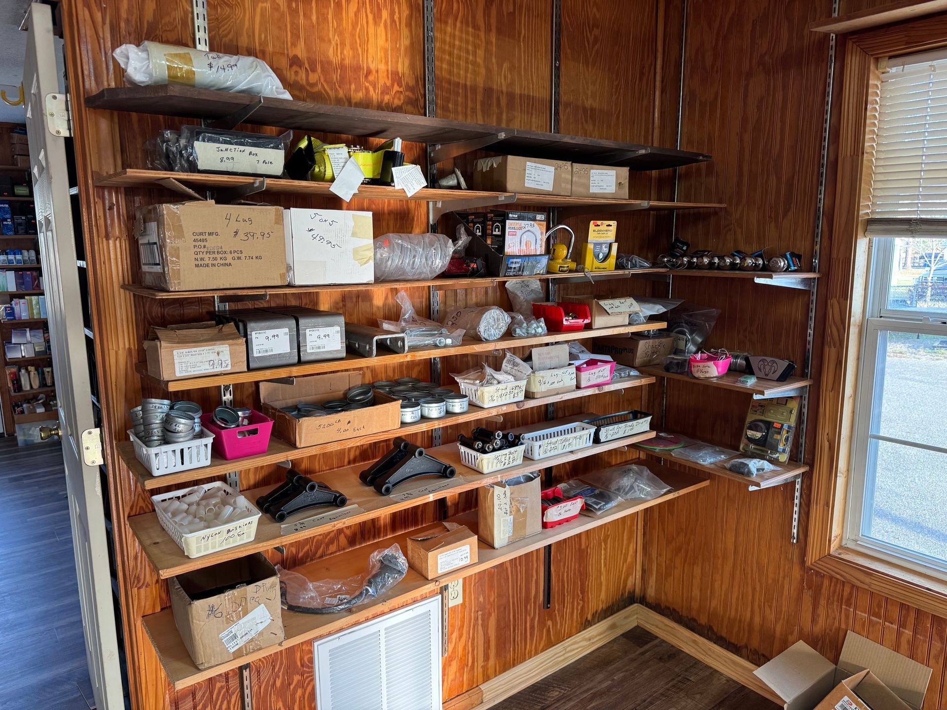 Wooden shelves on a paneled wall in a storage room are filled with assorted cardboard boxes, parts, and hardware.