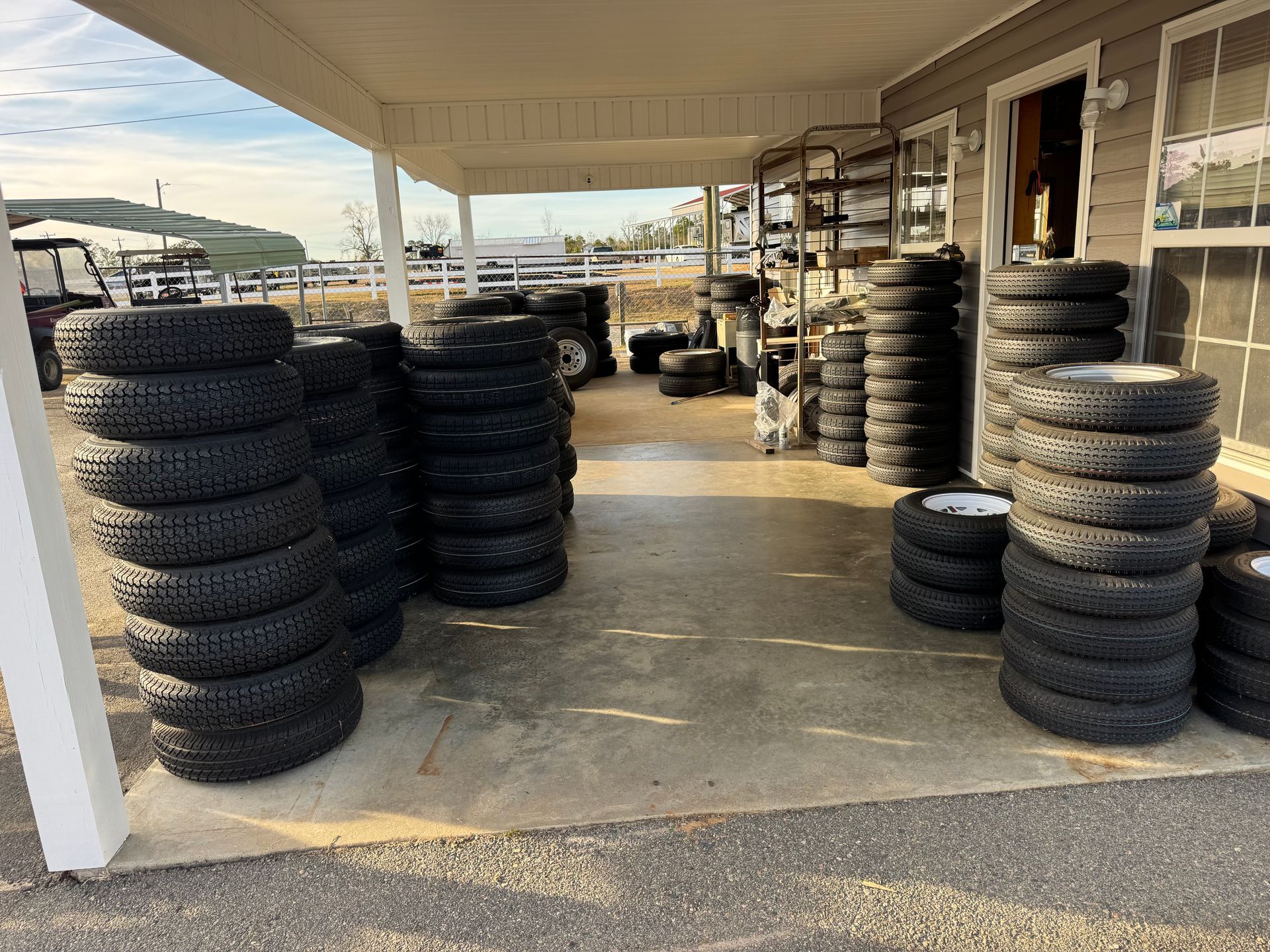 Stacks of black rubber tires lined up in rows under the covered porch of a workshop.
