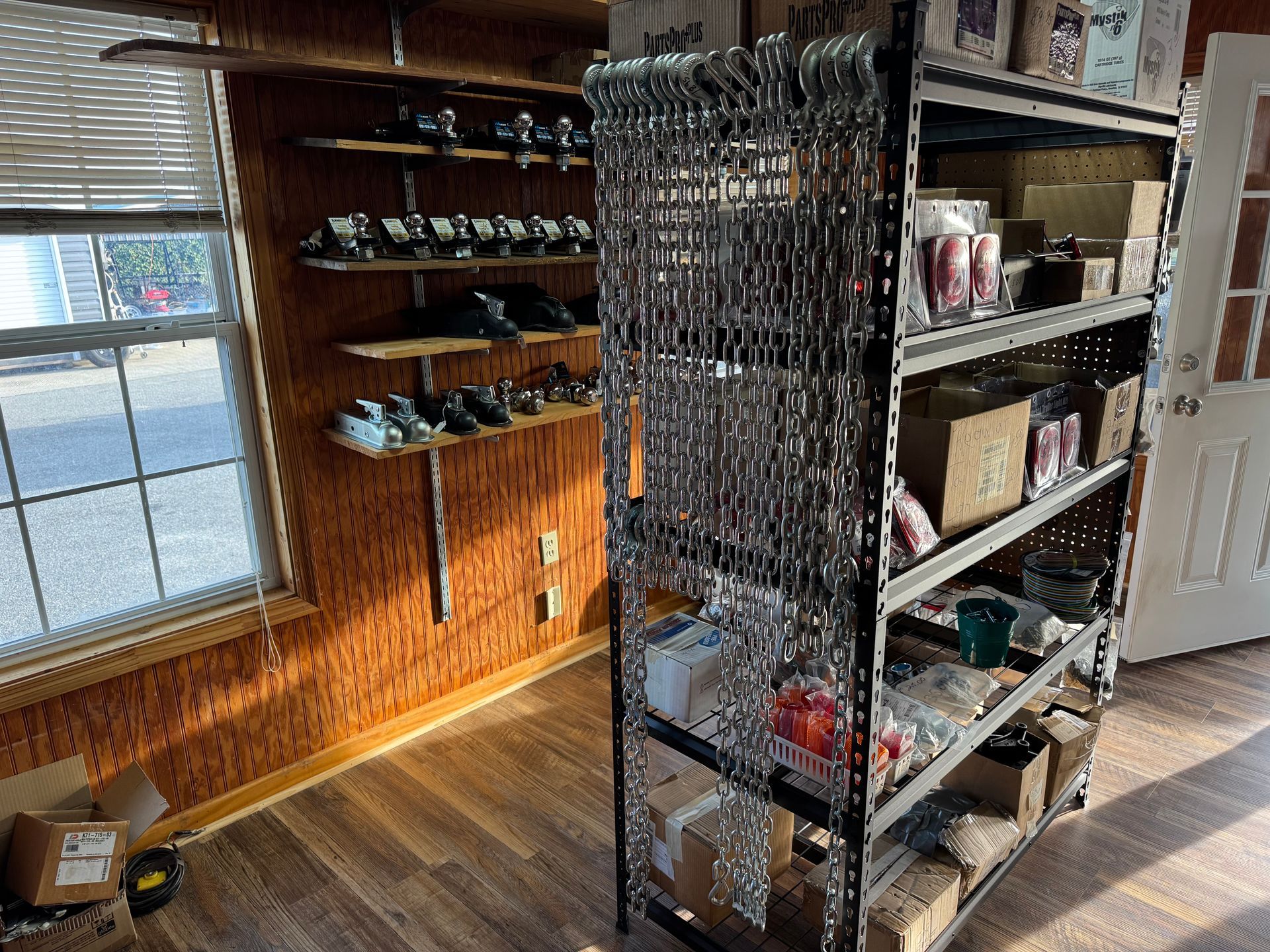 A hardware store interior with metal shelving units filled with chains, boxes, and items on wall-mounted shelves.