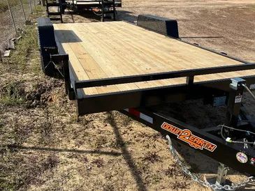 A flatbed utility trailer with a new wooden deck and black metal frame parked on a dirt lot.