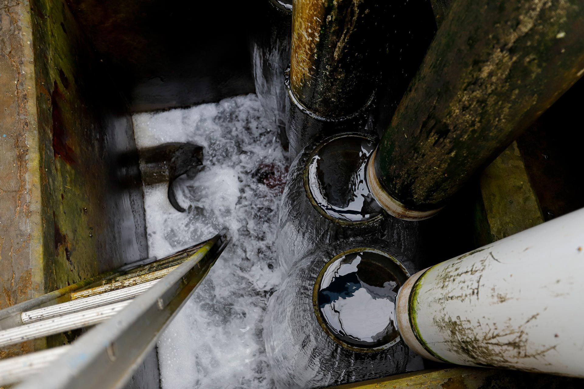 Top-down view of a wet industrial pit with pipes and foamy water accumulation