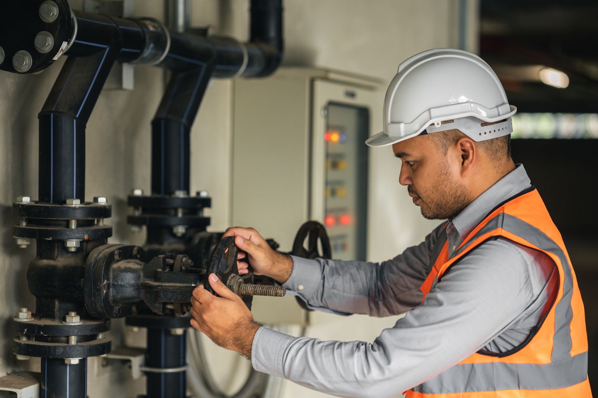 Technician in a hard hat and safety vest performing pump station repair on industrial valves and pip