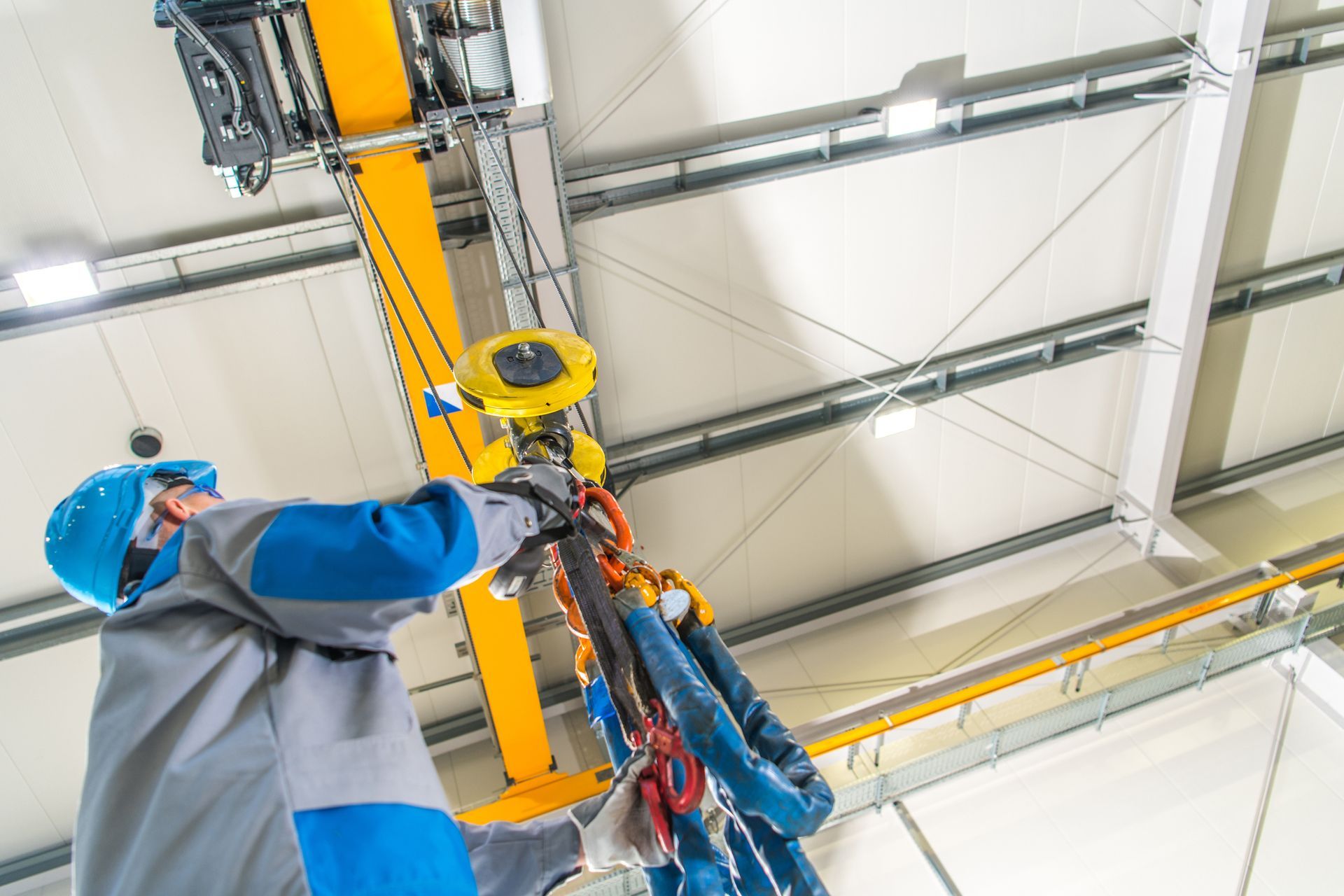 Worker in blue hard hat securing equipment on an overhead industrial lift inside a warehouse