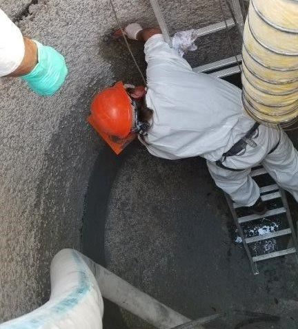 Lift Station Repairs Worker in orange hard hat working inside a narrow underground shaft beside pipes and a ladder
