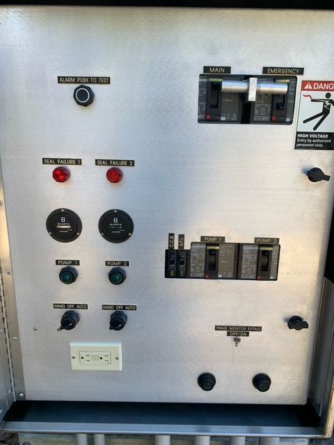Electrical control panel with switches, indicator lights, and circuit breakers on a gray cabinet.