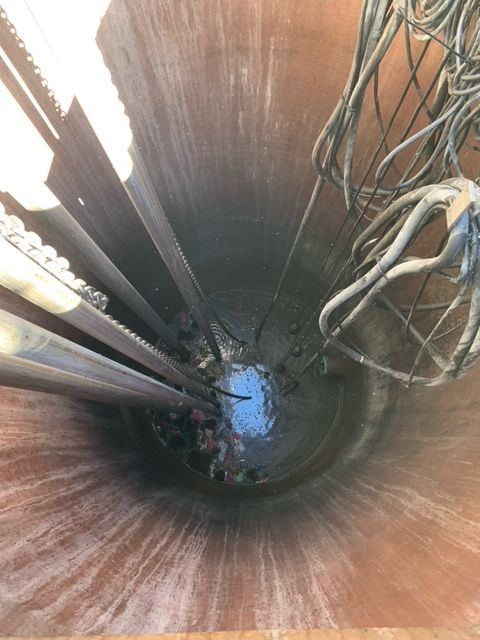 Looking down inside a deep cylindrical well with cables and pipes along the sides.