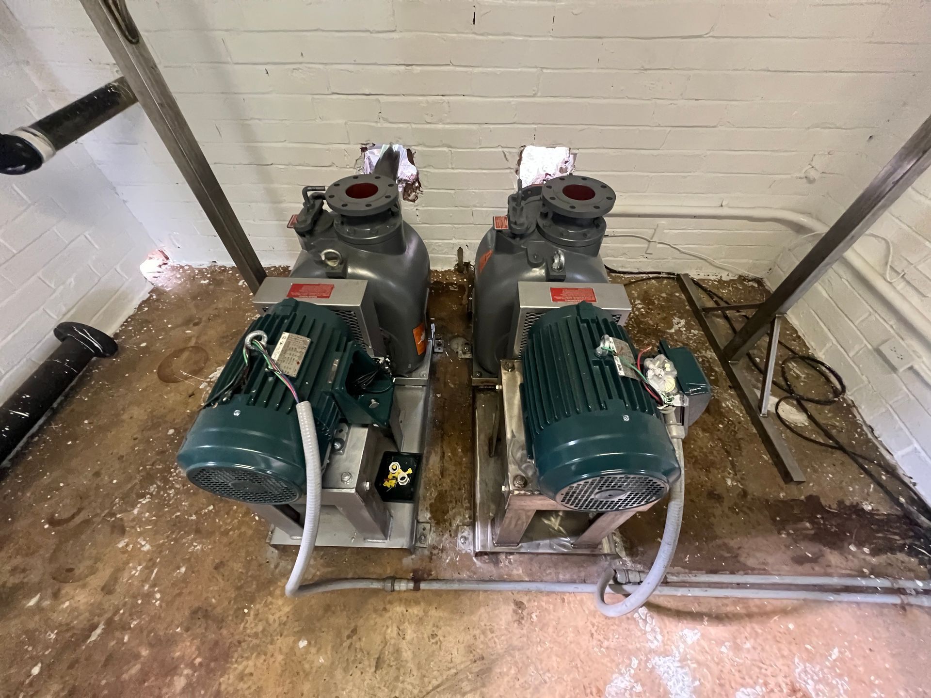 Two green industrial pumps mounted on a metal base in a utility room against a white wall