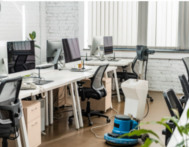 Modern office interior with workstations, computers, and cleaning equipment on the floor.
