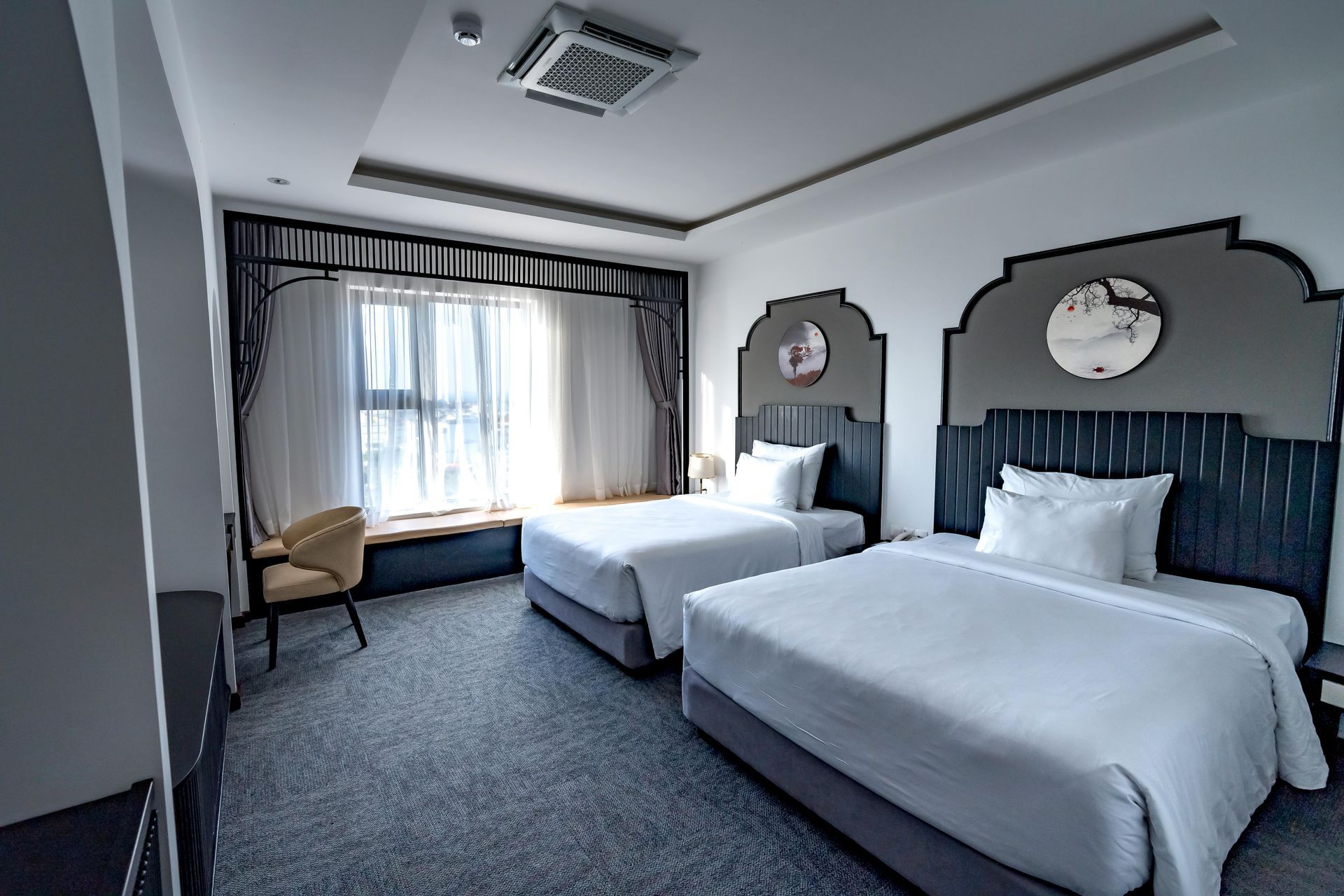 Hotel room with two twin beds, large window with curtains, and gray carpet.