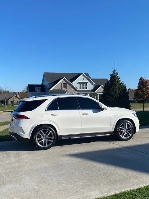 A white Mercedes-Benz GLE SUV parked on a concrete driveway in front of a suburban house under a clear blue sky.