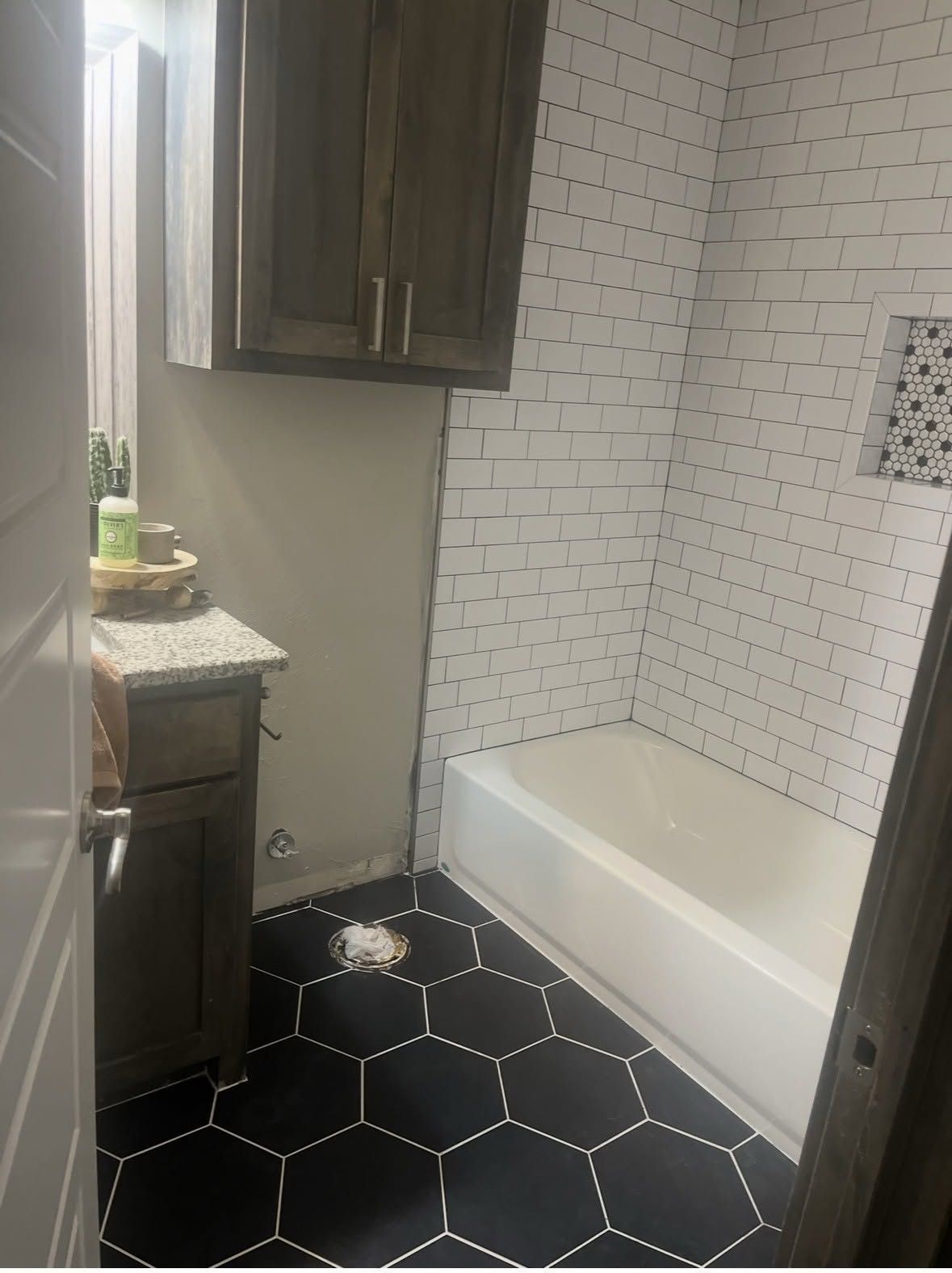 Small bathroom with black hex tile, white subway shower wall, and dark wood cabinets.