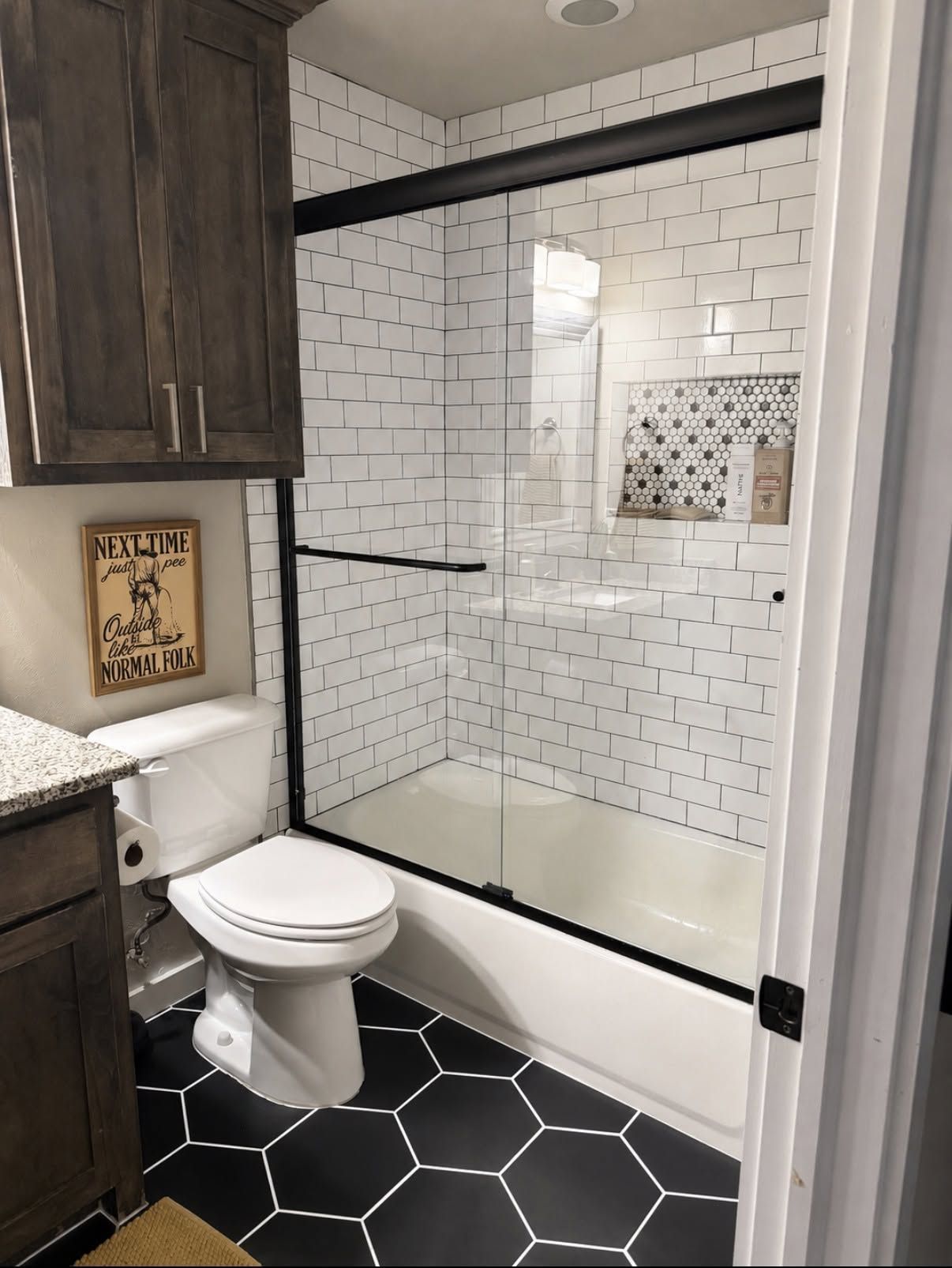 Small bathroom with glass shower, white subway tile, black hex floor, and toilet beside a cabinet.