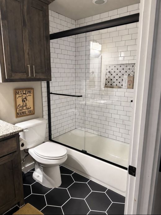 Small bathroom with glass shower, white subway tile, black hex floor, and toilet beside a cabinet.