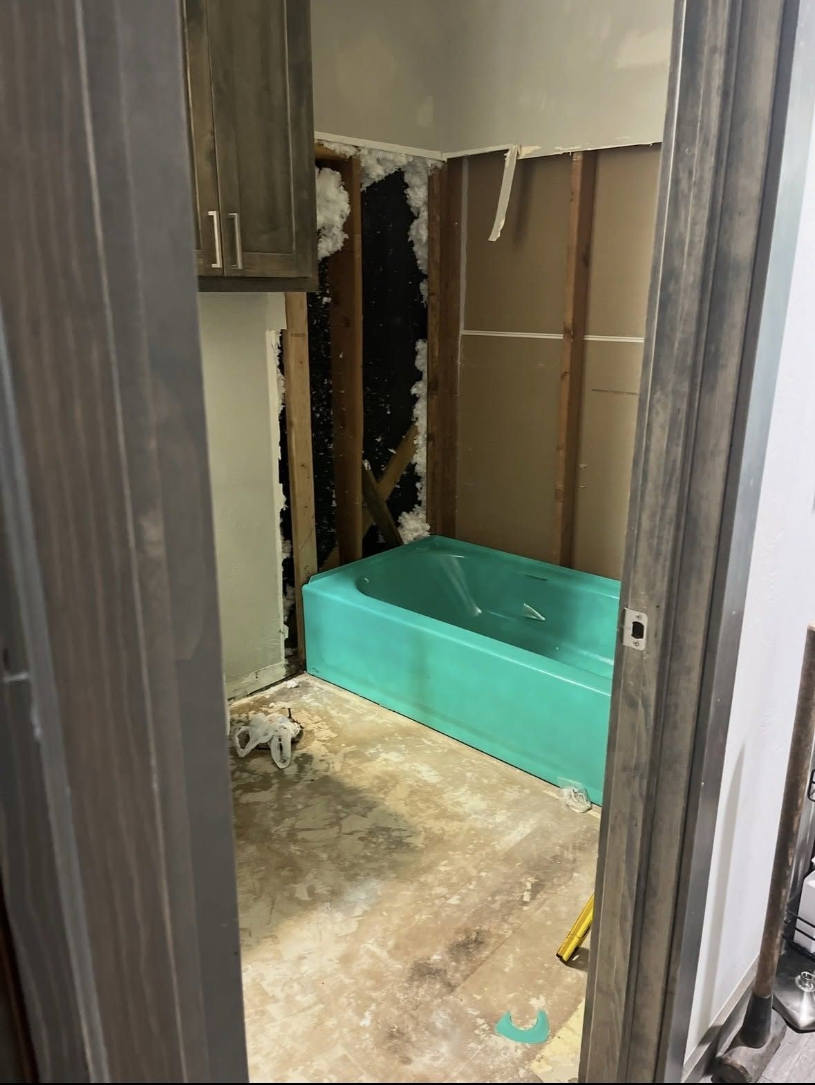 Damaged bathroom wall with exposed studs, torn drywall, and a turquoise bathtub or shower base.