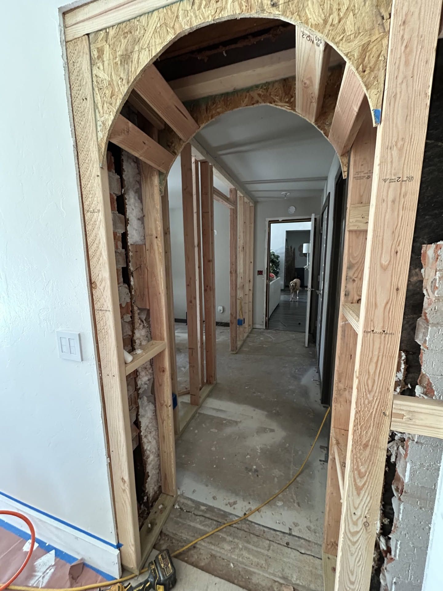 Partially renovated hallway with exposed wood framing and an arched doorway leading down the hall
