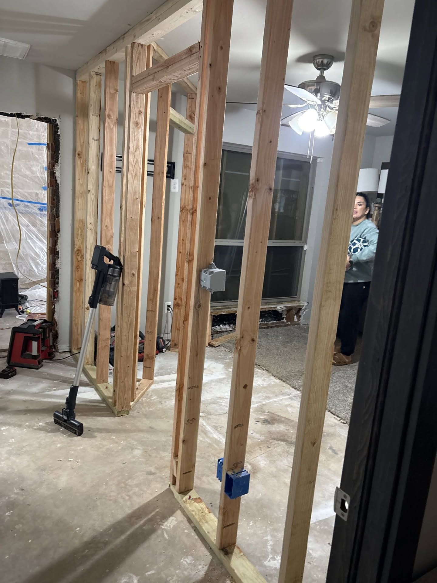 Interior under renovation with exposed wall studs, tools, and a person partially visible in the background.