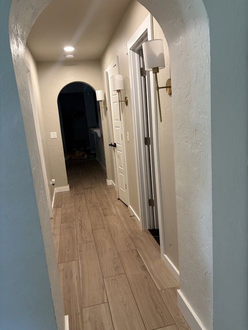 Narrow hallway with wood floor, white doors, and a dark arched doorway at the end.