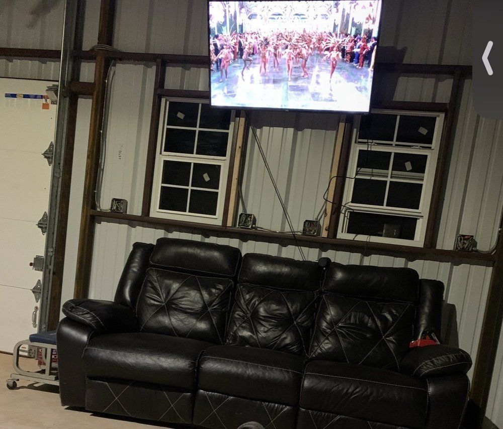 Black leather couch in a metal-walled room, with two windows and a TV showing a crowd above it.