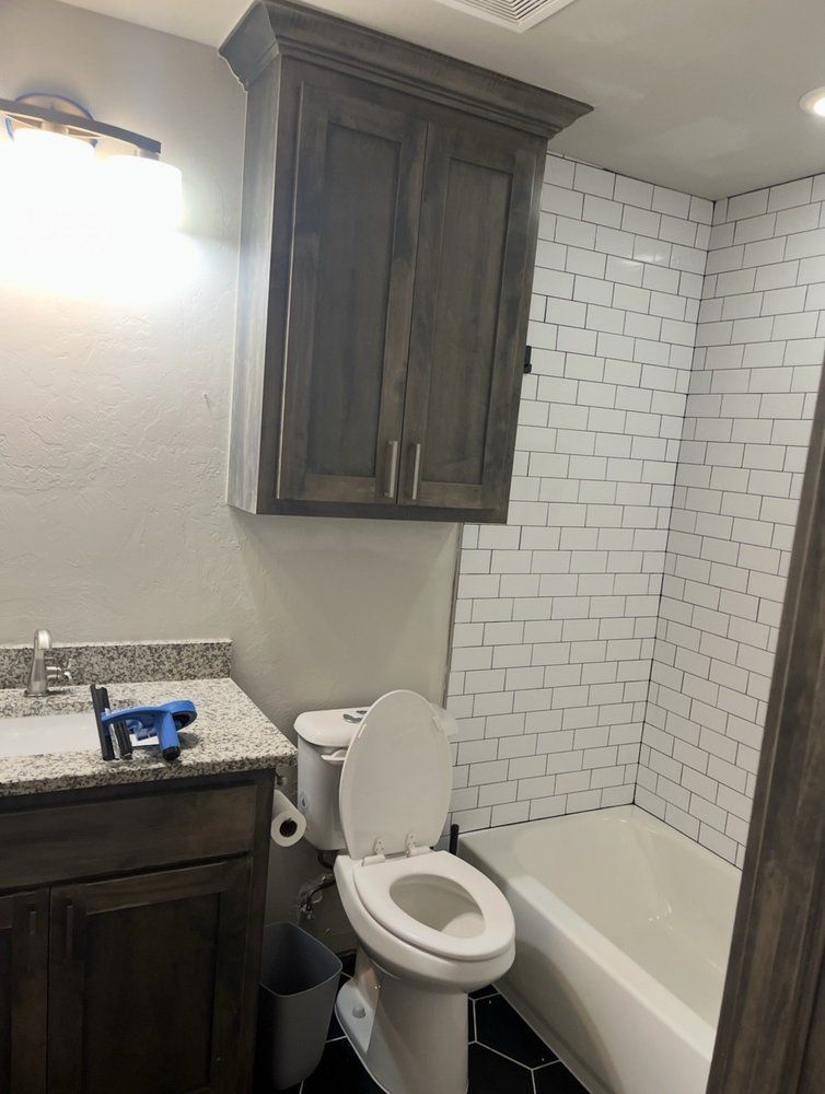 Small bathroom with toilet beside tub, dark wood cabinet, granite sink, and white subway-tile shower.