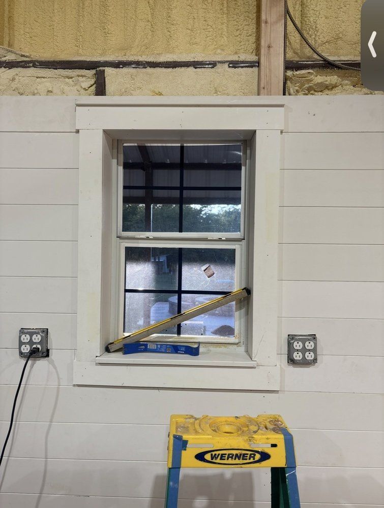 Small white-framed window in a workshop wall with a yellow tool on the sill and electrical outlets on both sides.