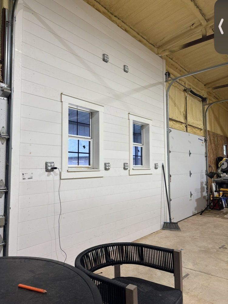 White industrial wall with two small windows in a warehouse-like space and a table and chair in the foreground