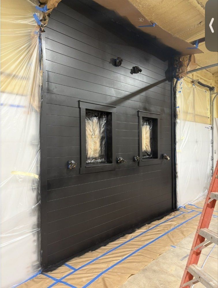 Black industrial-style door with two small windows in a construction area, with protective plastic sheeting around it.