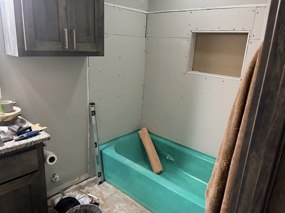 Small bathroom under renovation with green tub, unfinished drywall, and a towel hanging on the right.
