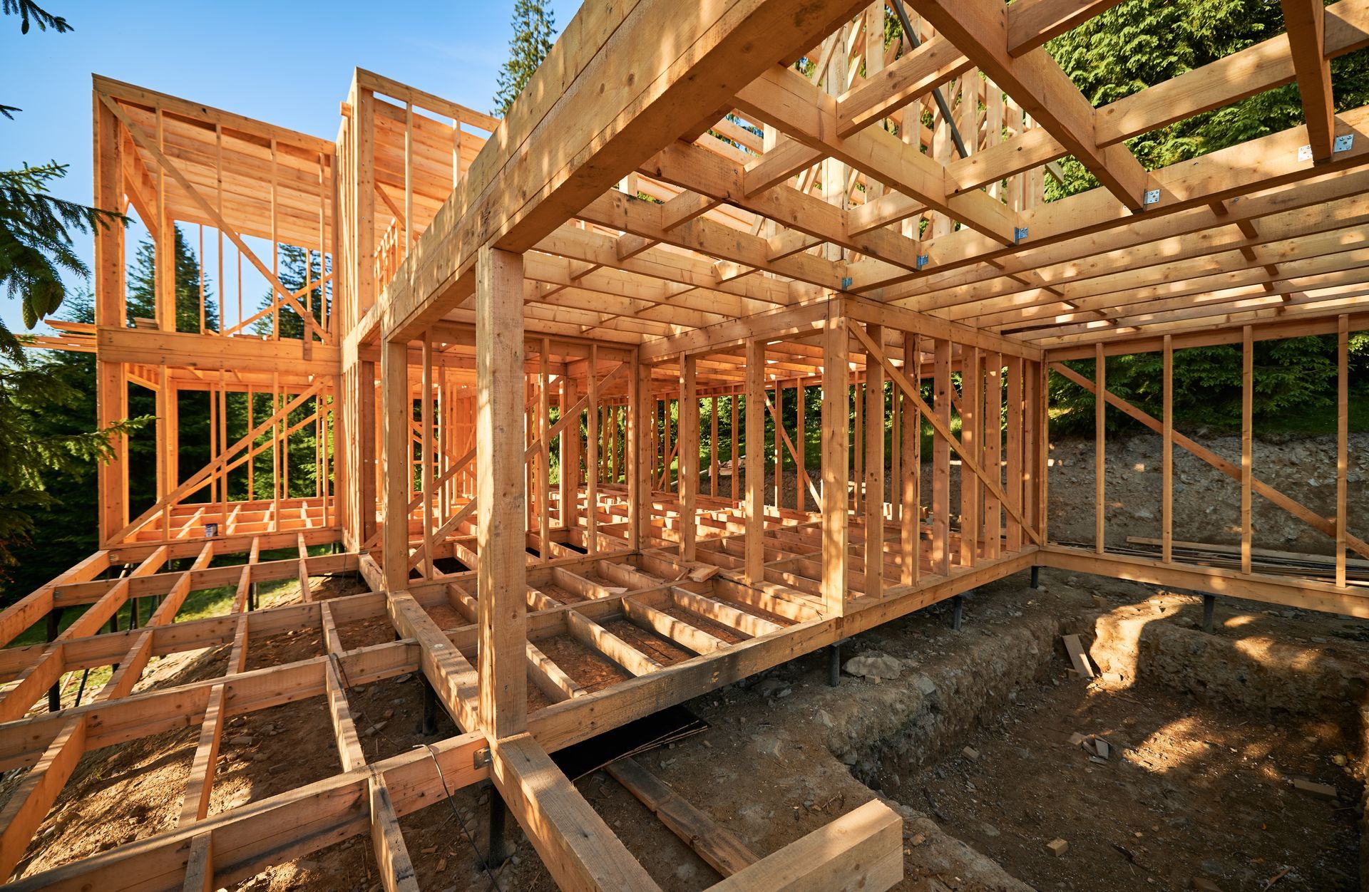 Wooden house framing under construction in sunlight, with open floor joists and wall studs