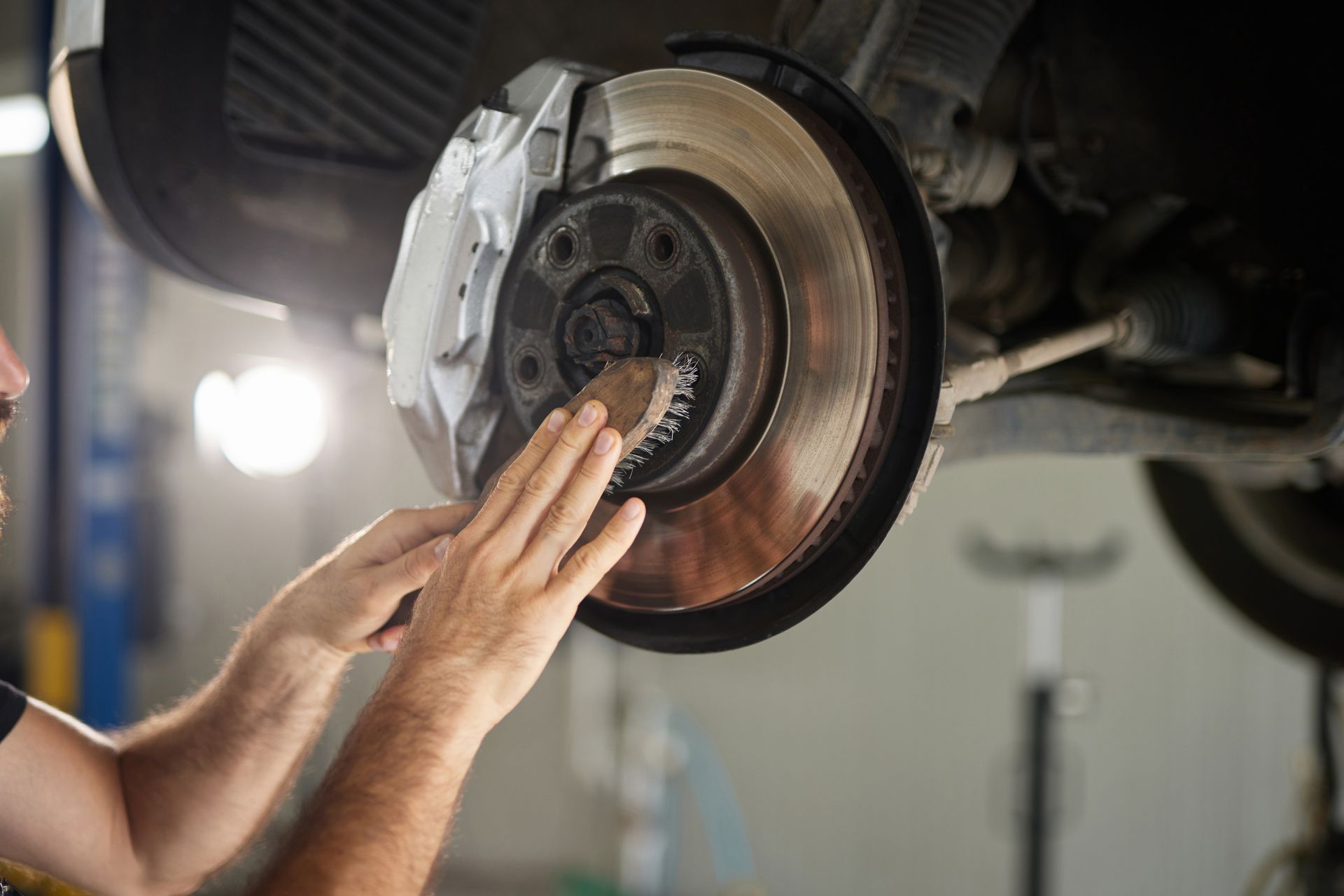 Mechanic inspecting a car brake rotor and caliper with hands in an auto repair shop