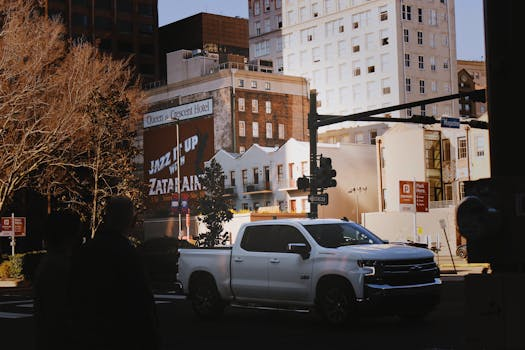 White pickup truck driving past brick buildings on a city street at dusk