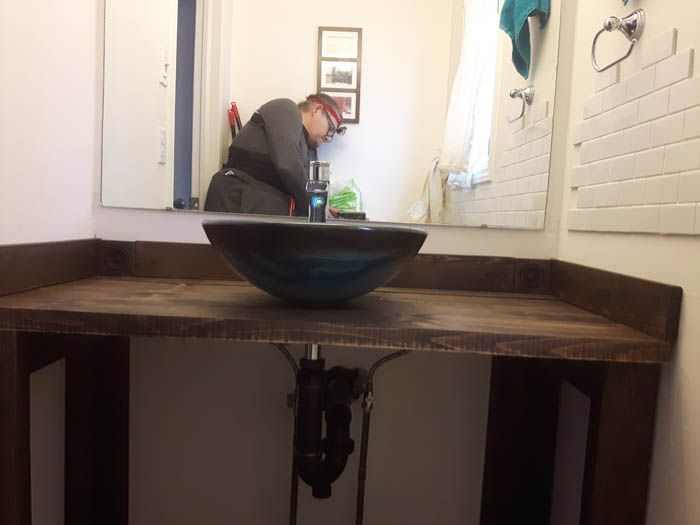 Une personne debout devant un miroir de salle de bains, travaillant à une coiffeuse dotée d'un comptoir en bois foncé et d'un lavabo vasque.
