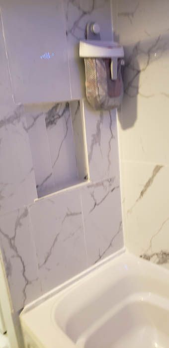Un mur de douche carrelé de carreaux à motif marbre blanc, avec une niche rectangulaire encastrée et un distributeur de savon mural.