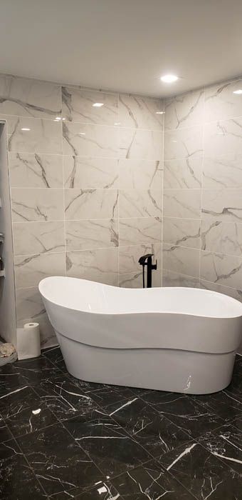 Une salle de bains moderne avec une baignoire îlot blanche, des murs carrelés de marbre et un sol en marbre foncé.