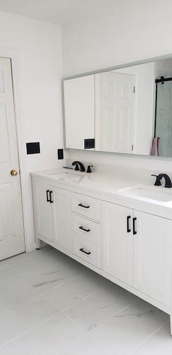 Un meuble-lavabo double blanc avec robinetterie noire et un grand miroir rectangulaire, adossé à un mur blanc.