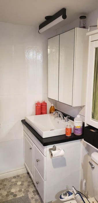 Un meuble-lavabo blanc avec un comptoir noir, un lavabo blanc, une armoire à miroir et un éclairage au plafond.