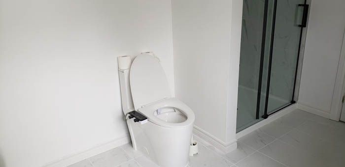 Des toilettes blanches avec siège de bidet intégré jouxtent une douche à parois de verre dans une salle de bains minimaliste aux murs blancs.