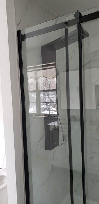 Une cabine de douche moderne avec un encadrement noir mat et une porte coulissante en verre contre un mur clair carrelé de marbre.