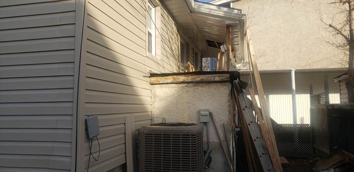 Vue extérieure d'un bâtiment au revêtement beige, avec un climatiseur et une échelle en bois appuyée contre celui-ci.