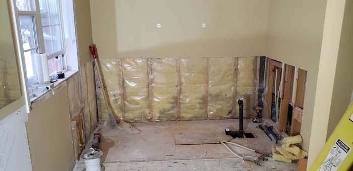 Une pièce en rénovation avec des cloisons sèches enlevées, des montants en bois apparents, une isolation jaune et une canalisation centrale.