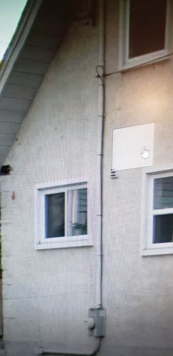 Vue latérale de l'extérieur d'une maison en stuc clair, montrant un compteur électrique et une gaine électrique remontant le long du mur.