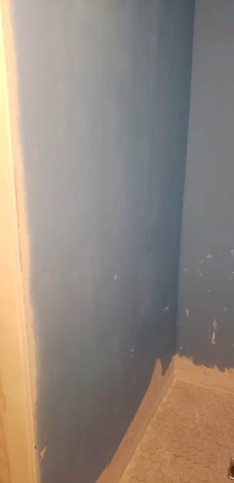 Un coin de pièce aux murs peints en bleu, au-dessus d'une plinthe beige inachevée.