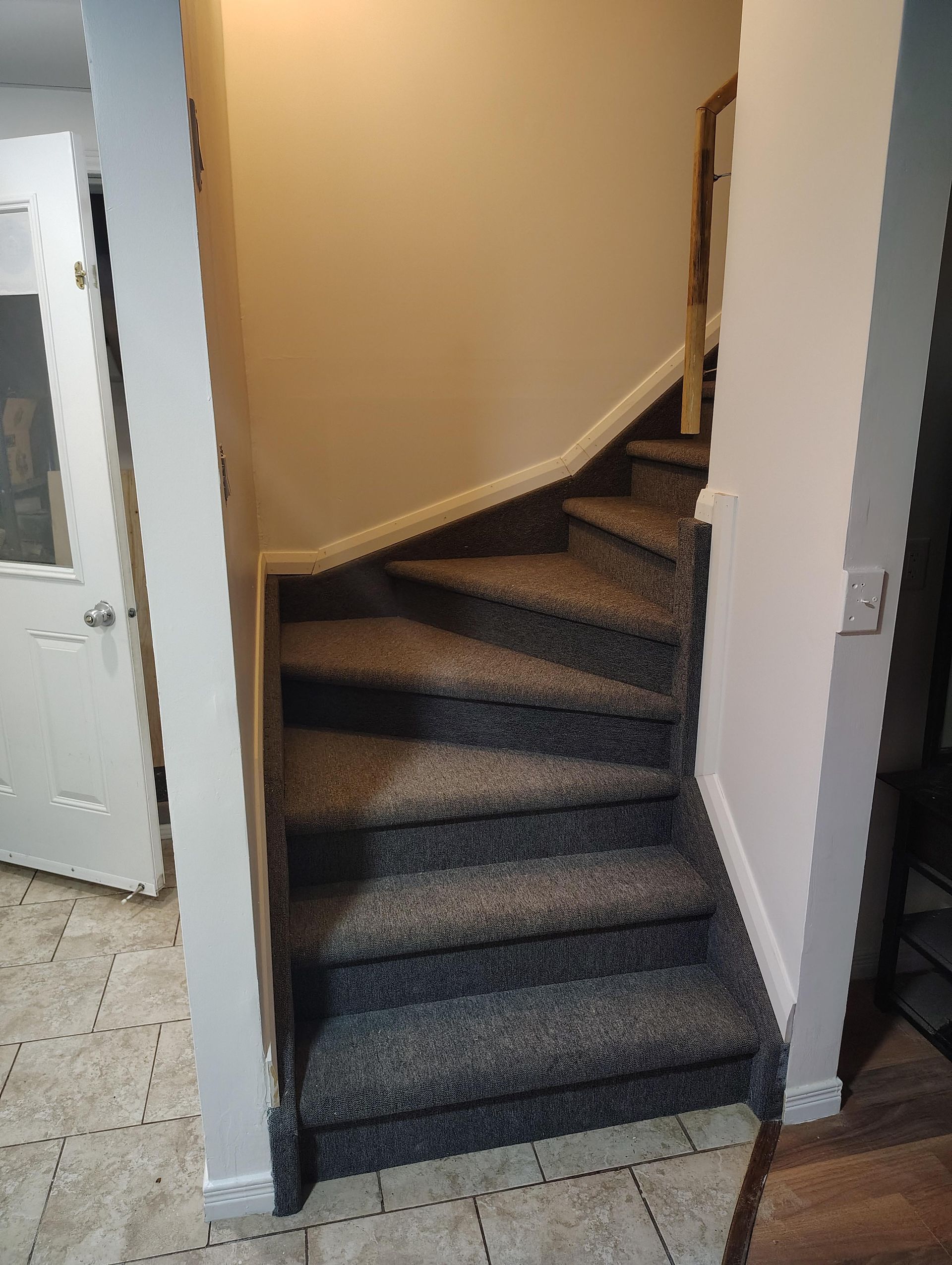 Un escalier recouvert de moquette, avec un palier incurvé, est bordé de murs blancs dans un couloir intérieur.
