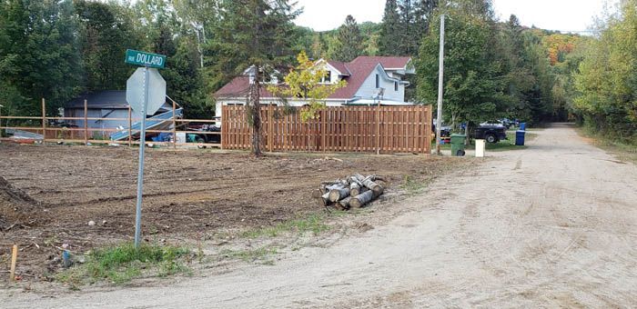 Un carrefour de chemin de terre avec un panneau stop, une clôture en bois et une maison dans un cadre rural.