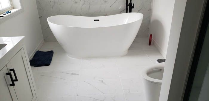 Une salle de bains moderne avec une baignoire îlot blanche, un sol en marbre, un meuble-lavabo blanc et des toilettes.