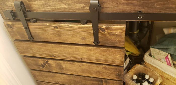 Une porte d'armoire en bois avec des ferrures coulissantes en métal rustique et des roulettes fixées sur un rail, partiellement ouverte pour montrer son contenu.