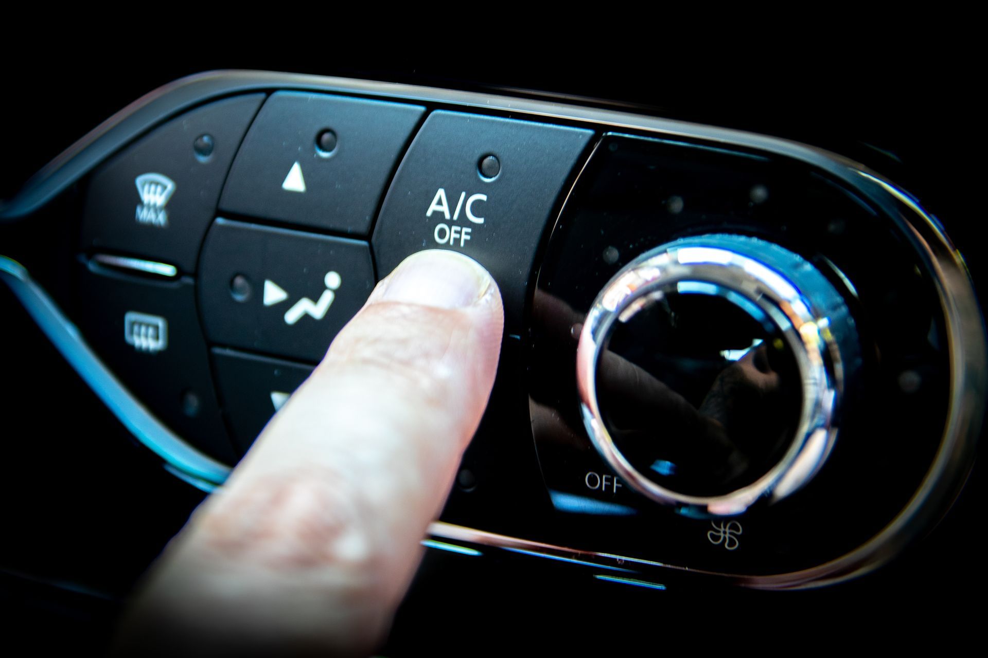 A finger presses the A/C Off button on a car's black climate control dashboard.
